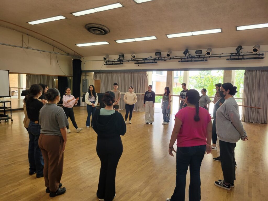 Cinthia Durán teaching a Latin social dance class in a circle, UC Riverside Department of Dance studio