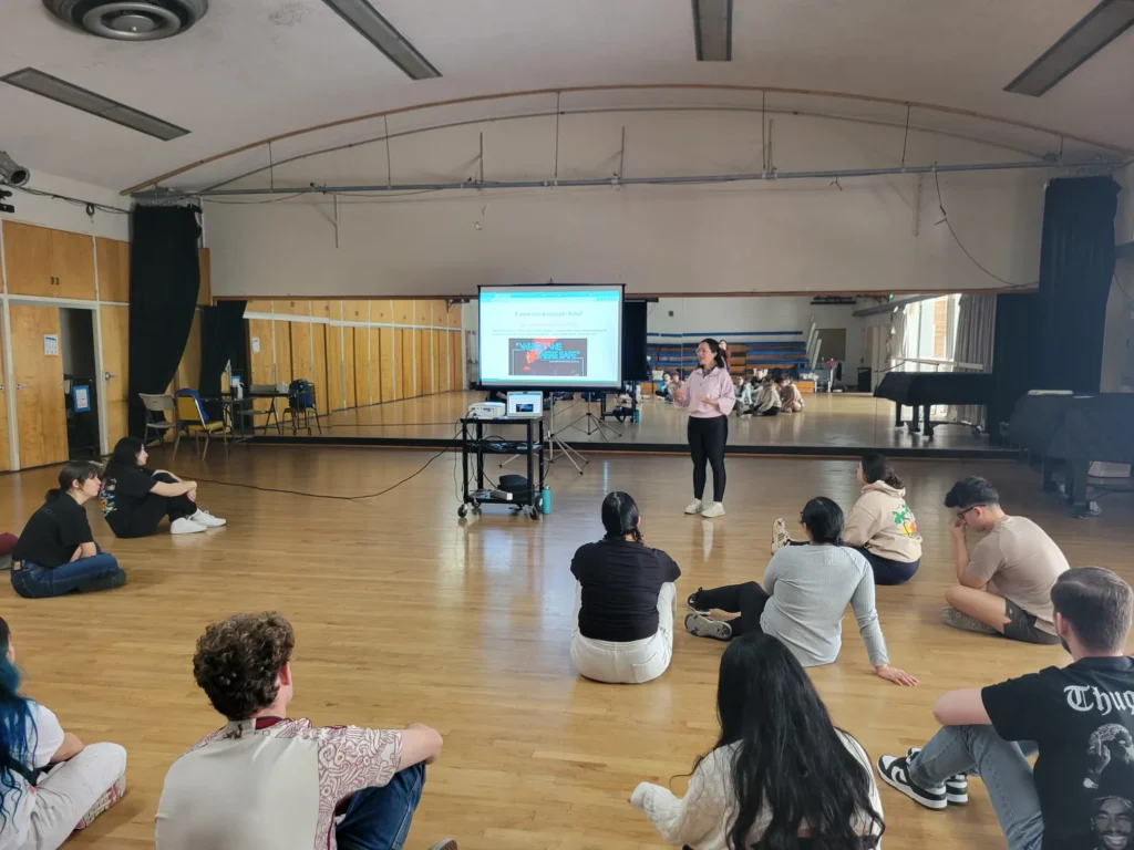 Cinthia Durán presenting beside an upright piano in a dance studio
