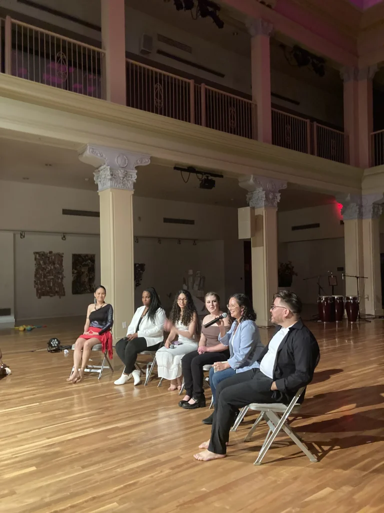 Panel discussion on stage with congas and hand percussion in the background