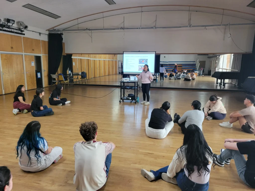 Students seated in a circle on the studio floor during a presentation